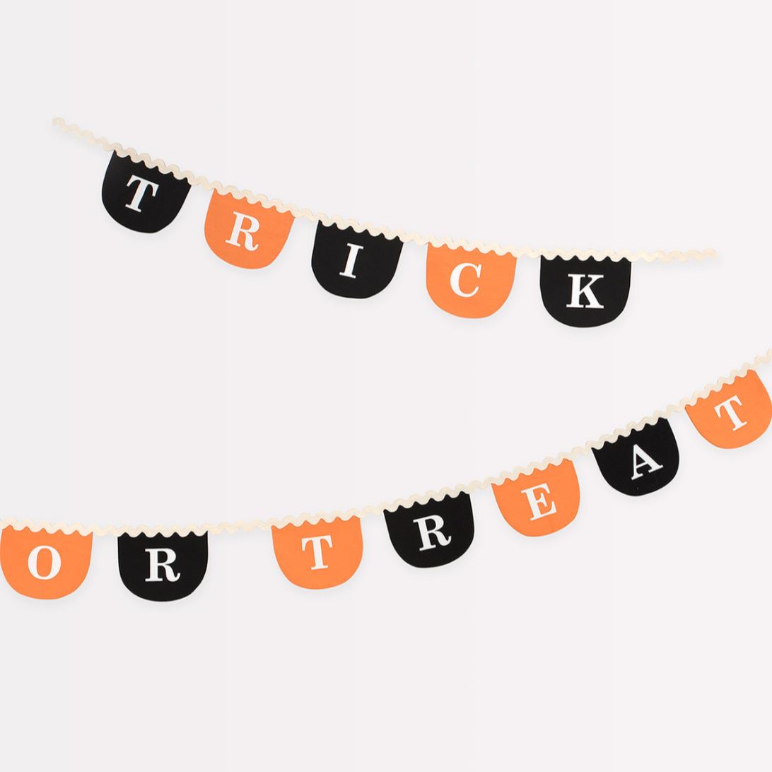 A fabric garland with the text 'TRICK OR TREAT' printed in black on orange background with ric rac details, scalloped shapes, and white screen printed letters.