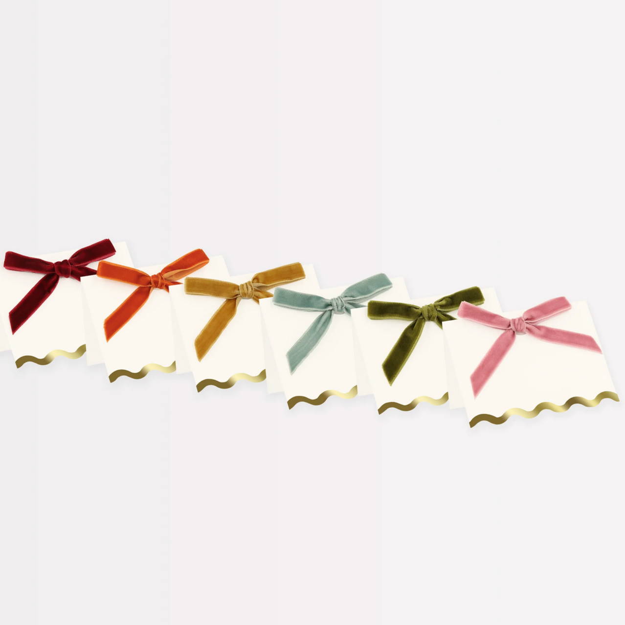 A set of placecards with scalloped edges and different colored velvet bows including golden yellow, burnt orange, teal blue, dusty pink, olive green, and deep red.