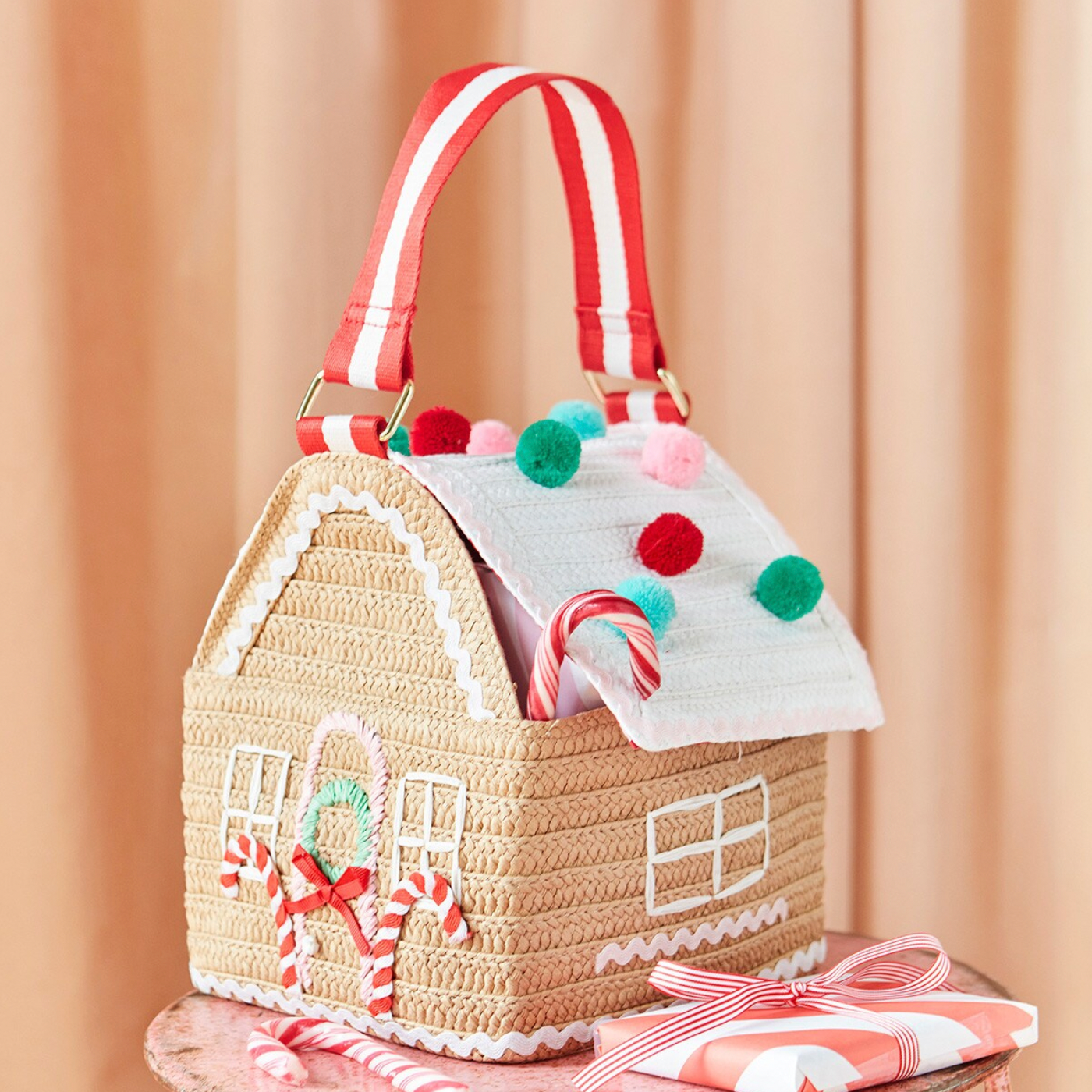 A woven paper bag designed to resemble a gingerbread house, with decorative details in red, white, and green, including a roof that opens and closes with a magnetic closure, and a handle for carrying.