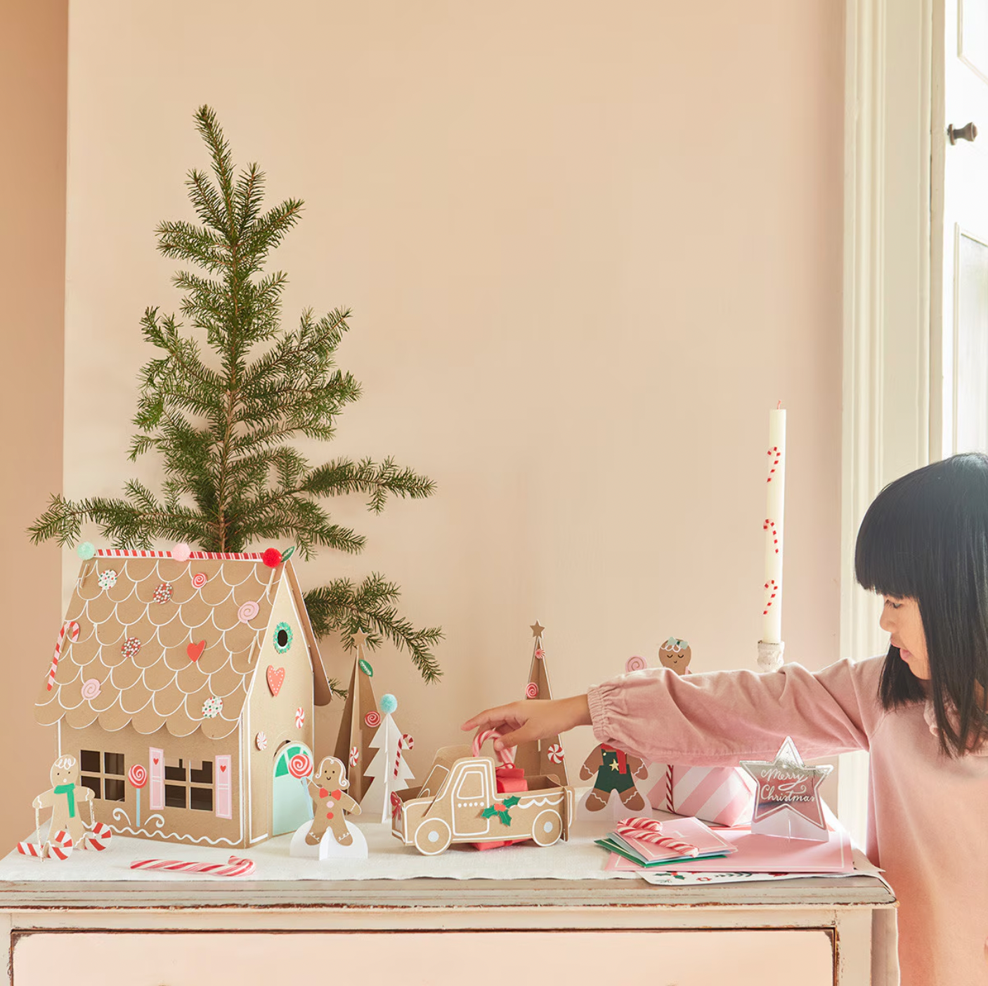 A child is assembling a gingerbread-themed sticker advent calendar which includes various flat gingerbread pieces and yarn pompoms to decorate a festive scene.