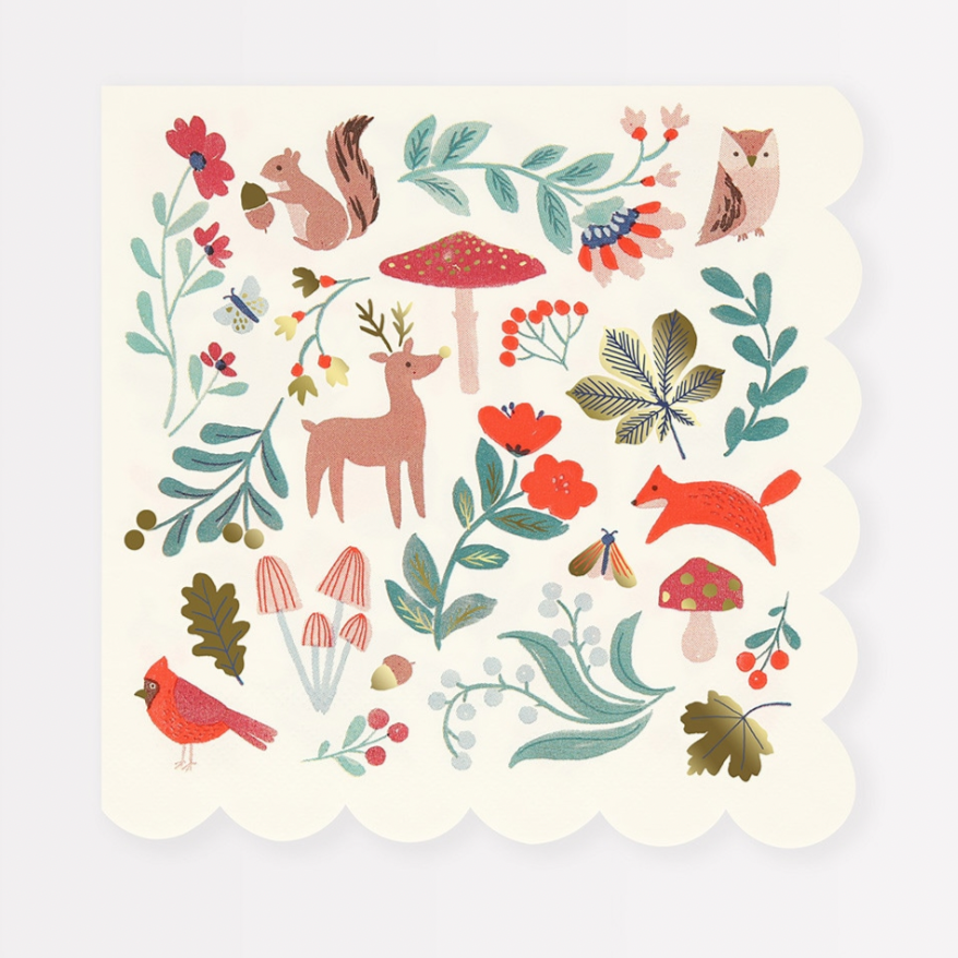 A festive napkin with a winter woodland theme, featuring illustrations of reindeer, squirrels, mushrooms, and berries, adorned with shiny gold foil details.