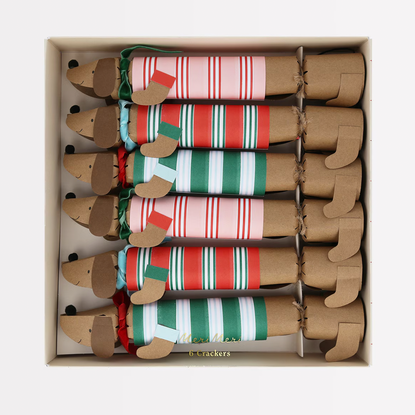 A set of six sausage dog-shaped crackers with festive stripe designs, each adorned with a velvet ribbon scarf in light blue, dark green, and red, and black pompom noses. The crackers are displayed in an open box, showing the festive items inside.