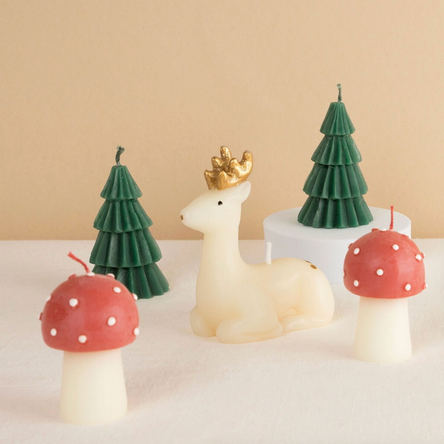A set of five decorative candles featuring a reindeer, Christmas tree, and mushroom designs, with white tissue paper wrapping and gold and black finishes.