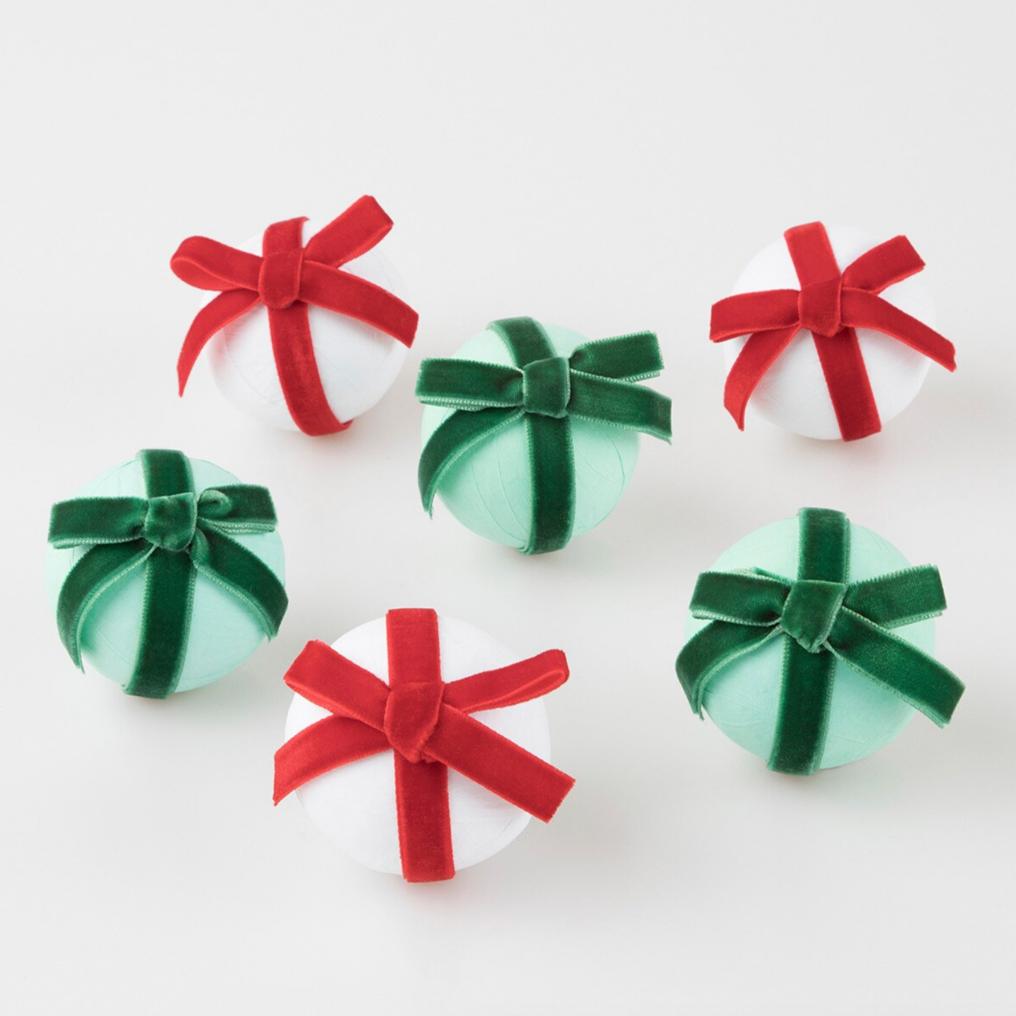 A set of six surprise balls with bows, three with white crepe paper and red velvet ribbons, and three with mint crepe paper and green velvet ribbons.