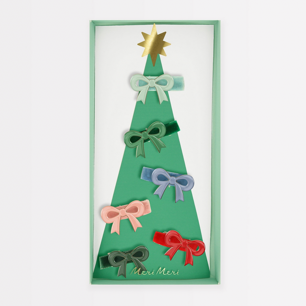 A set of six enamel bow hair clips in various colors including red, pink, blue, green, and dark green, presented on a paper Christmas tree backing with a shiny gold foil star.
