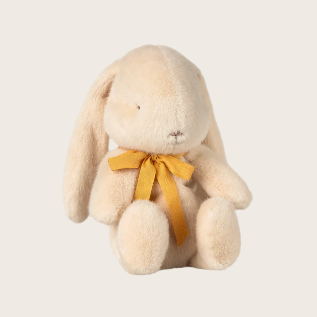 A small beige plush toy in the shape of a rabbit with a yellow bow around its neck.