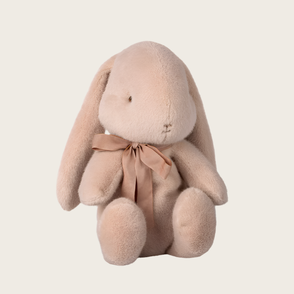 A soft plush toy in the shape of a bunny with a bow around its neck, in a light pink color.