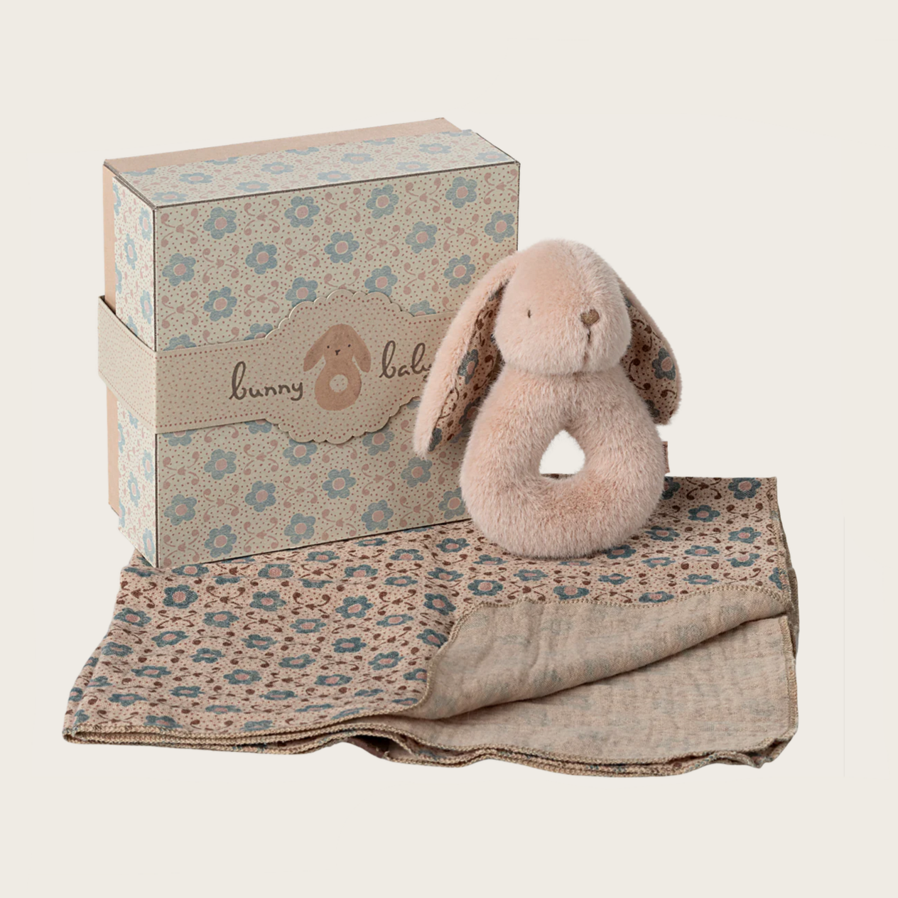 A soft cotton cloth with a floral pattern alongside a small beige rabbit rattle with a pink inner ear and a bow tie, presented in a matching floral gift box.