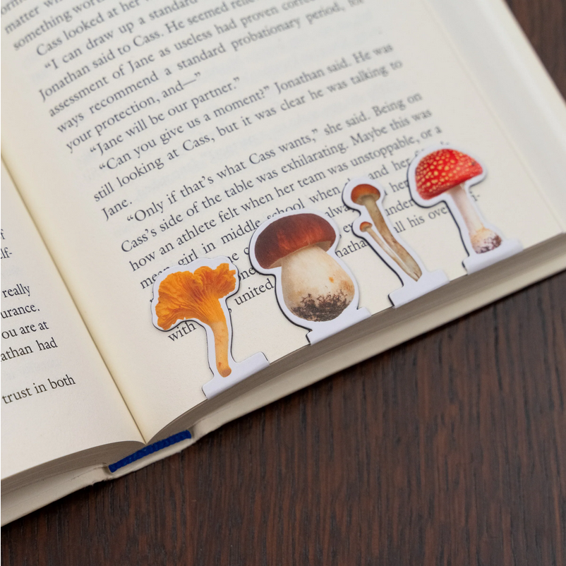 Open book with mushroom illustrations bookmarks on a wooden surface