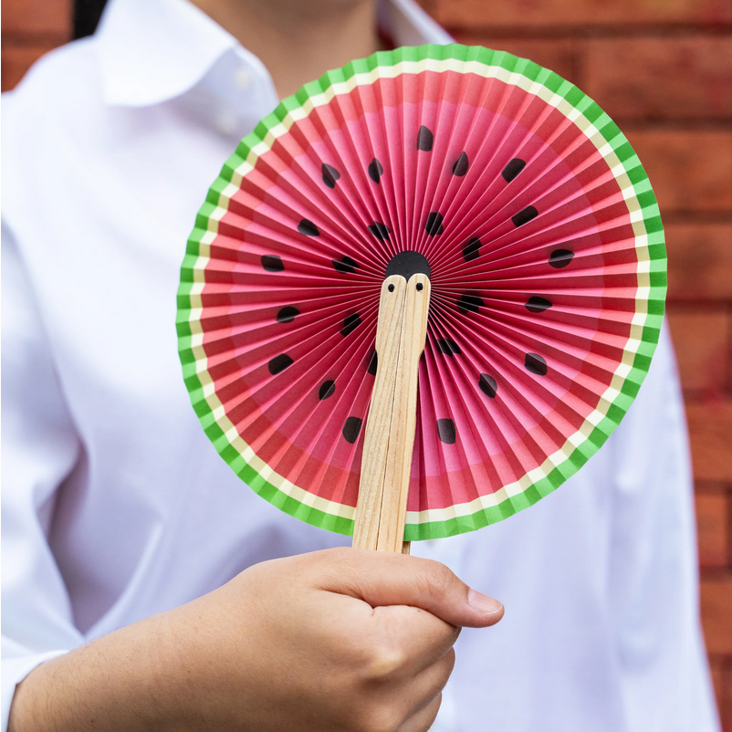 Hand holding a paper fan designed to look like a watermelon slice.