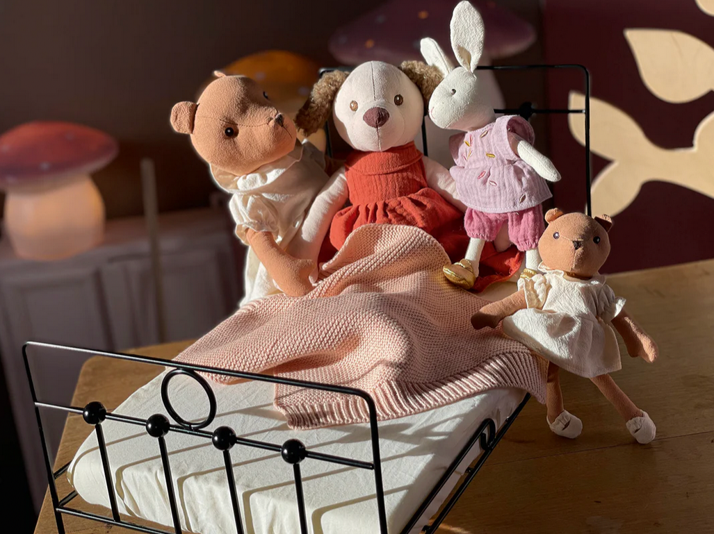 Four stuffed animals on a small bed with a pink blanket in a cozy room.