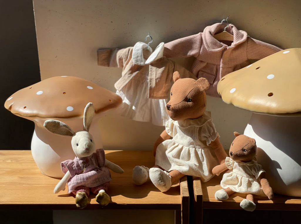 Three plush toys on a wooden shelf with mushroom-shaped lamps in the background.