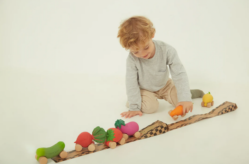 Child playing with a wheeled food cars on a white background