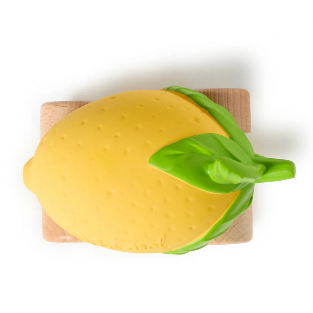 Yellow lemon-shaped object with green stem on a wooden cutting board against a white background
