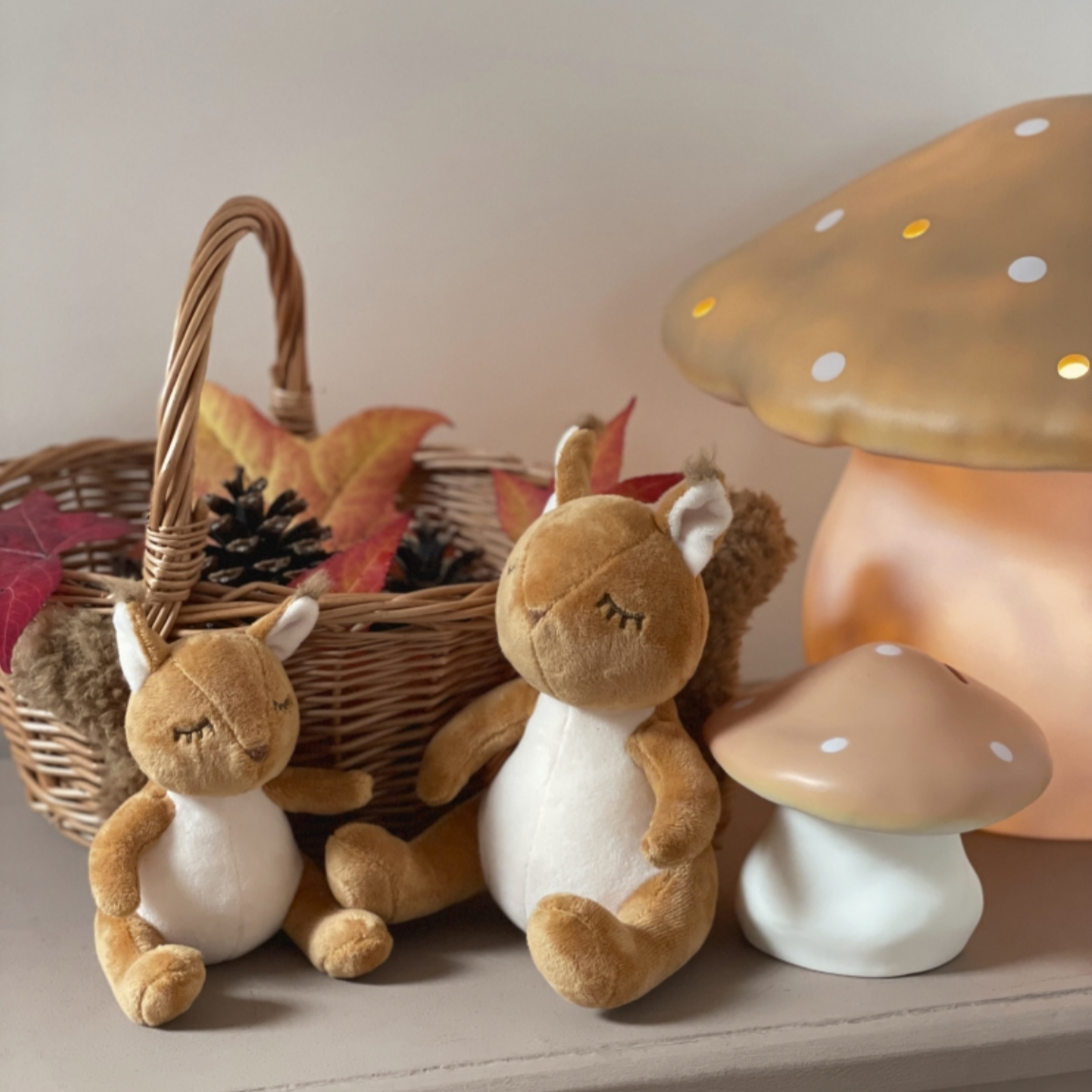 Two plush animals, a basket with leaves, and a mushroom-shaped lamp on a surface.