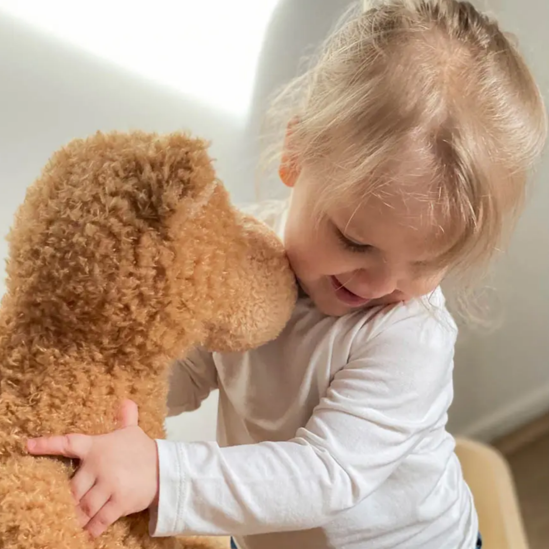 Child hugging a brown teddy bear indoors