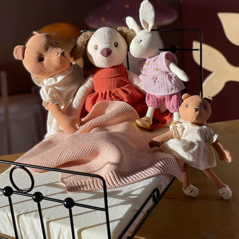 Four stuffed animals on a small bed with a soft focus background