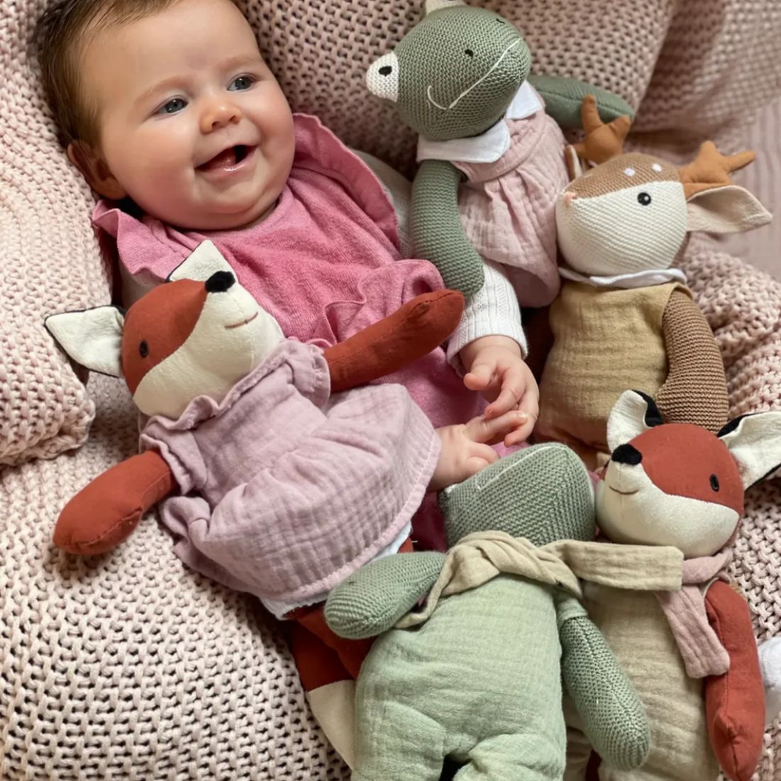 Baby surrounded by plush toys on a soft surface