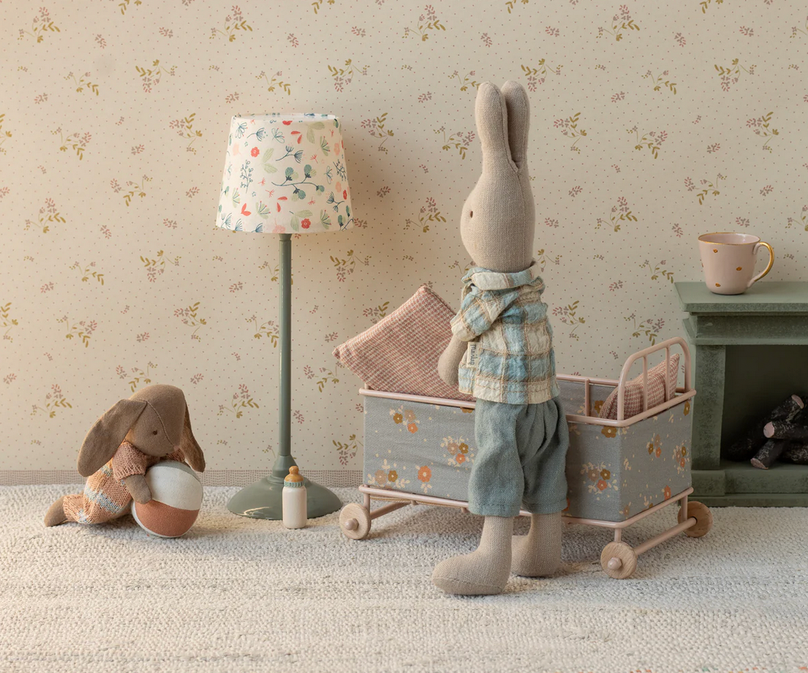 Children's room with stuffed rabbit, lamp, and toys against floral wallpaper.