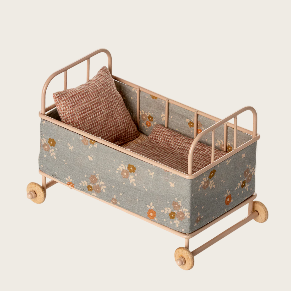 Small doll bed with floral pattern and brown cushions on a beige background
