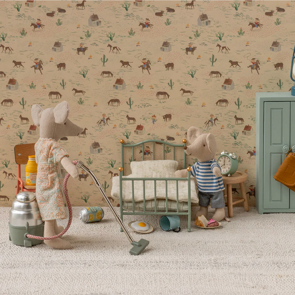 Miniature scene with toy mice in a room setting against a patterned wallpaper.