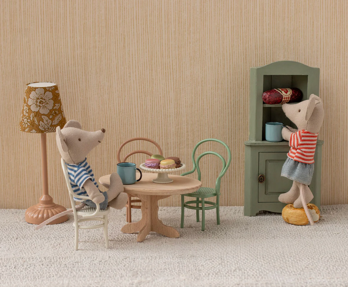 Miniature scene with toy mice around a table, including a lamp and cabinet, against a striped wall.