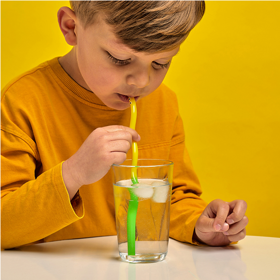 Child drinking from a glass with a straw against a yellow background