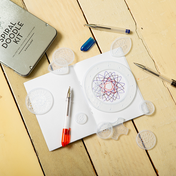 Spiral doodle kit with templates, pens, and a completed design on a wooden surface