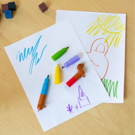 Colorful markers on a piece of paper with child-like drawings on a wooden surface