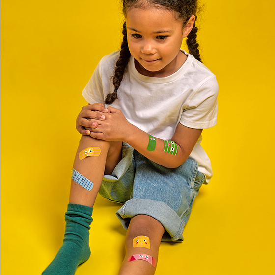Child with colorful band-aids on a yellow background