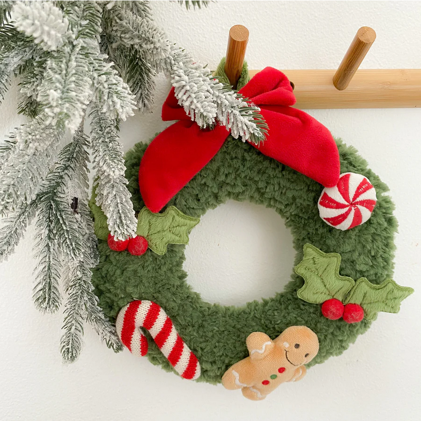 Decorative Christmas wreath with a red bow, candy cane, gingerbread man, and holly leaves on a white background.