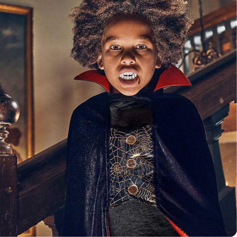 Child in a Halloween costume with a dark cape and red collar, standing on a staircase.