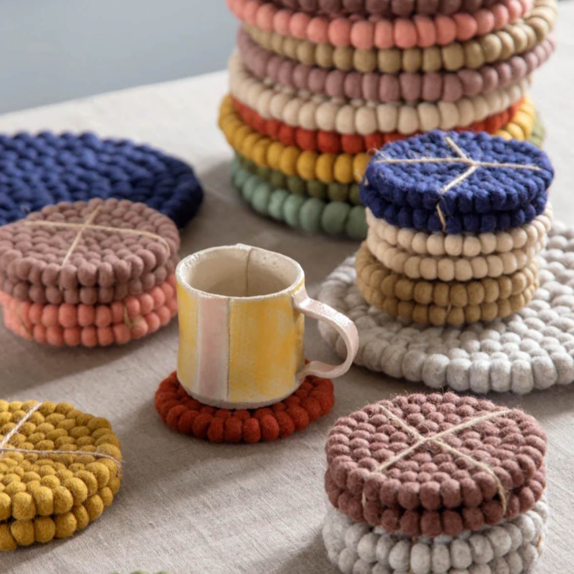 Colorful woven coasters on a table with a mug.