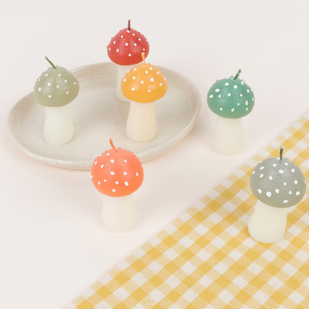Colorful mushroom-shaped candles on a white plate with a yellow checkered tablecloth.