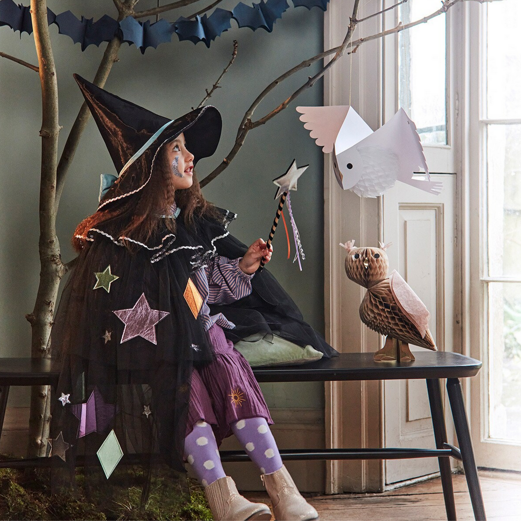 Child in a witch costume sitting on a bench with Halloween decorations.
