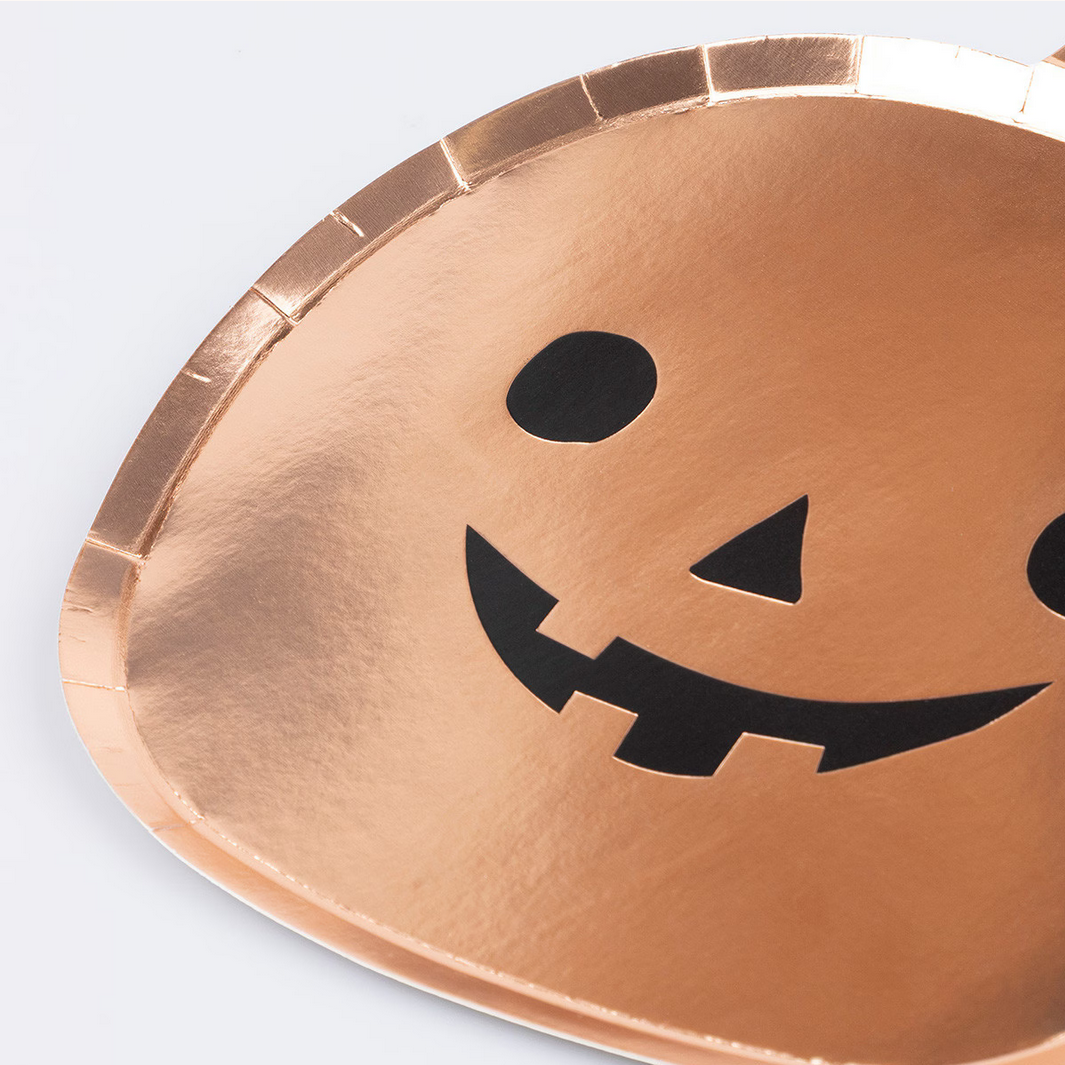 Copper-colored paper plate with a jack-o'-lantern face design on a light gray background