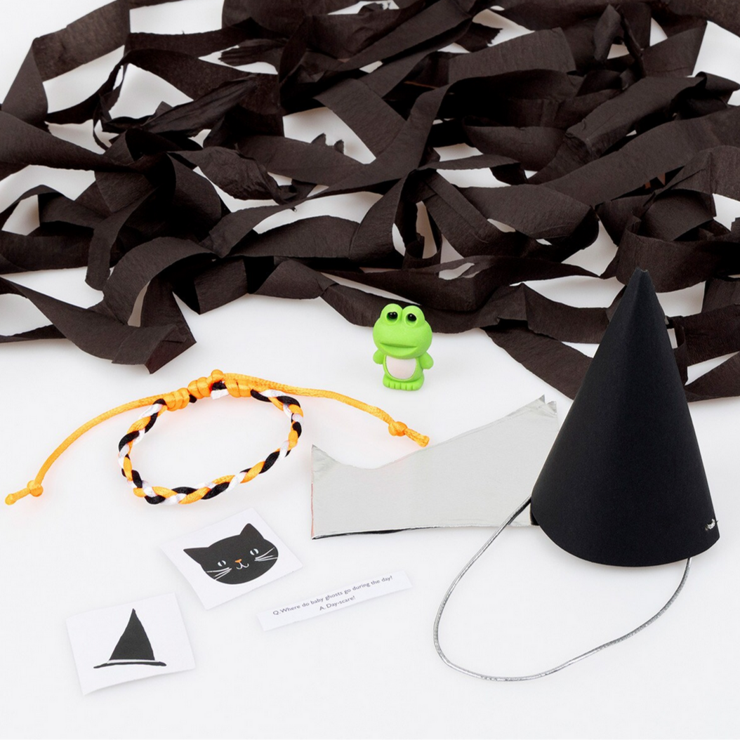 Halloween-themed items including black paper bats, a black party hat, and a green frog toy on a white background.