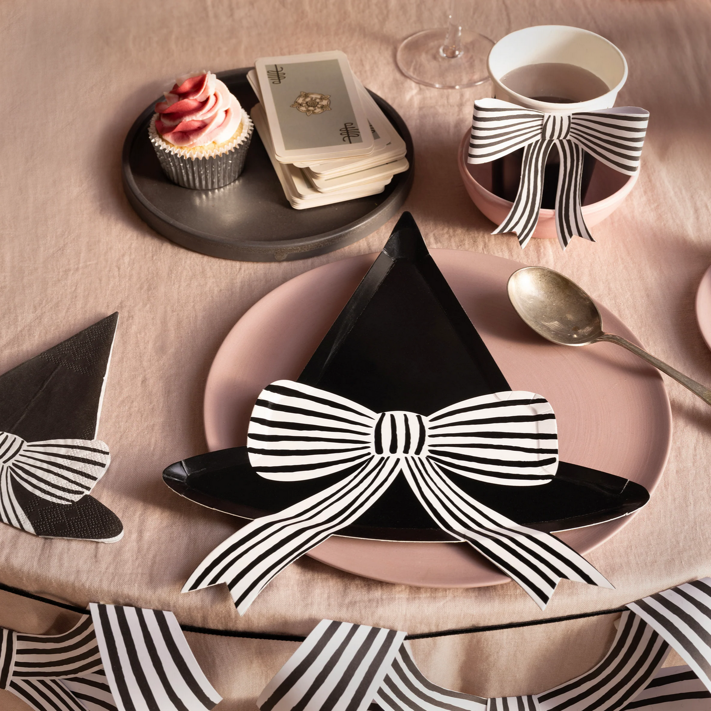 Table setting with black napkins and striped bow decorations on a pink tablecloth.