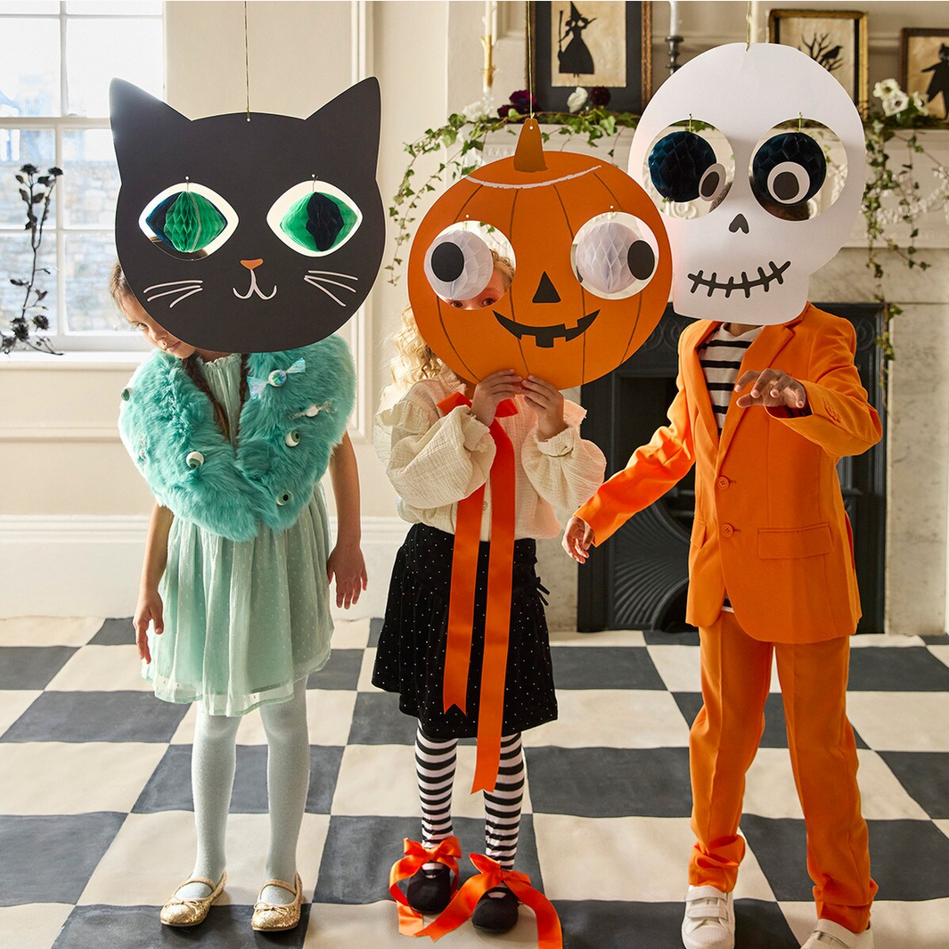 Three children behind Halloween-themed cardboard decorations in a room with a checkered floor.