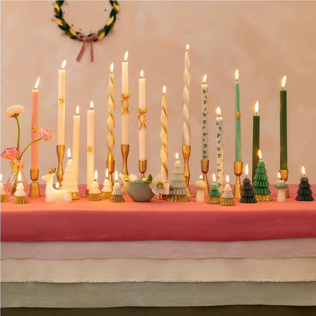 Diverse collection of candles on a table with a pink tablecloth.