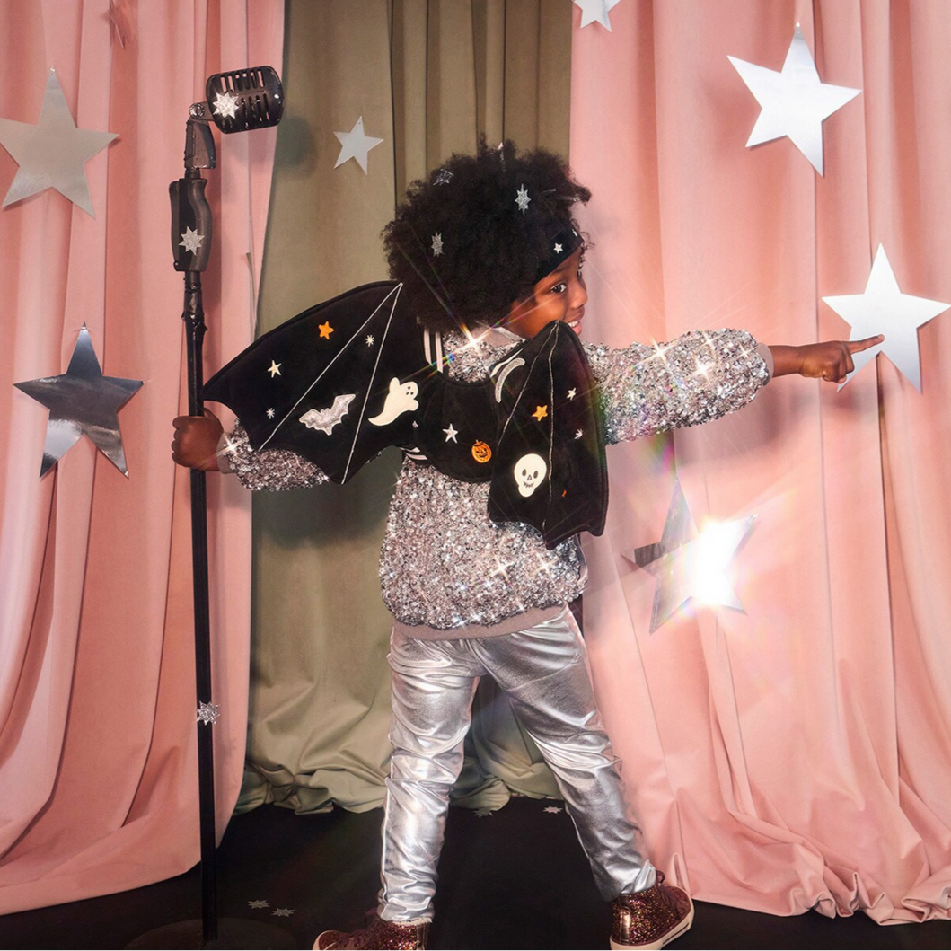 Child in a sparkly outfit with a bat wings costume against a pink curtain backdrop.