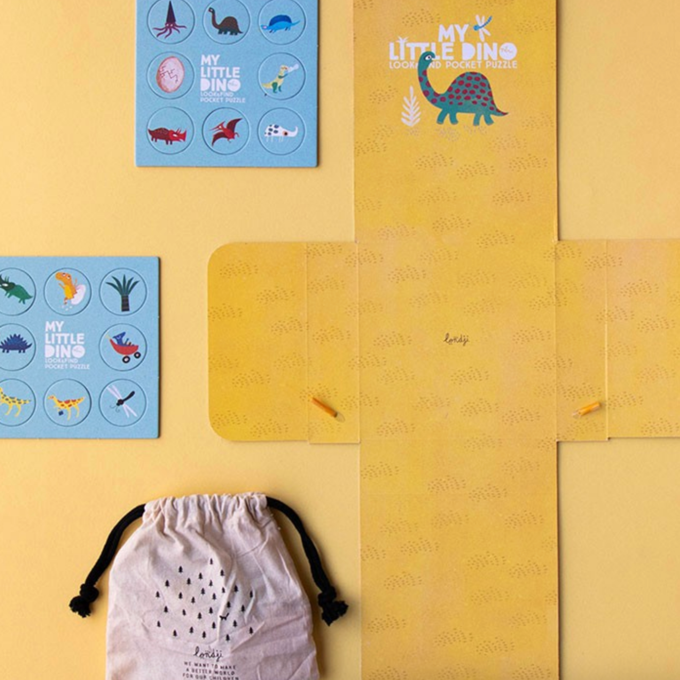 Children's dinosaur-themed products including a pouch, cards, and a mat on a yellow background.