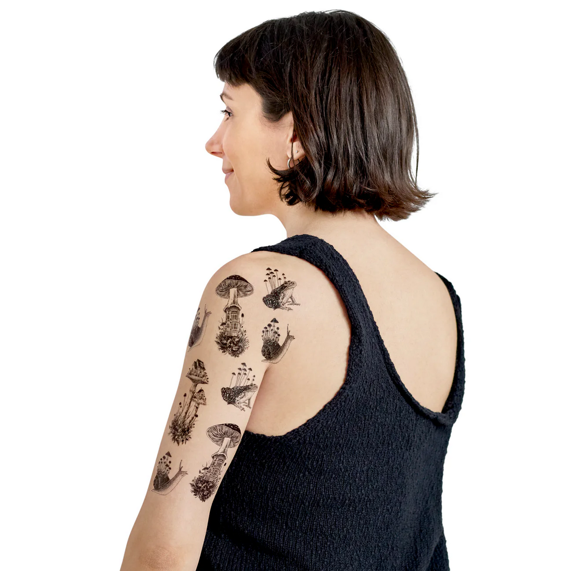 Woman with black sleeveless top and tattoos on her arm and shoulder against a white background