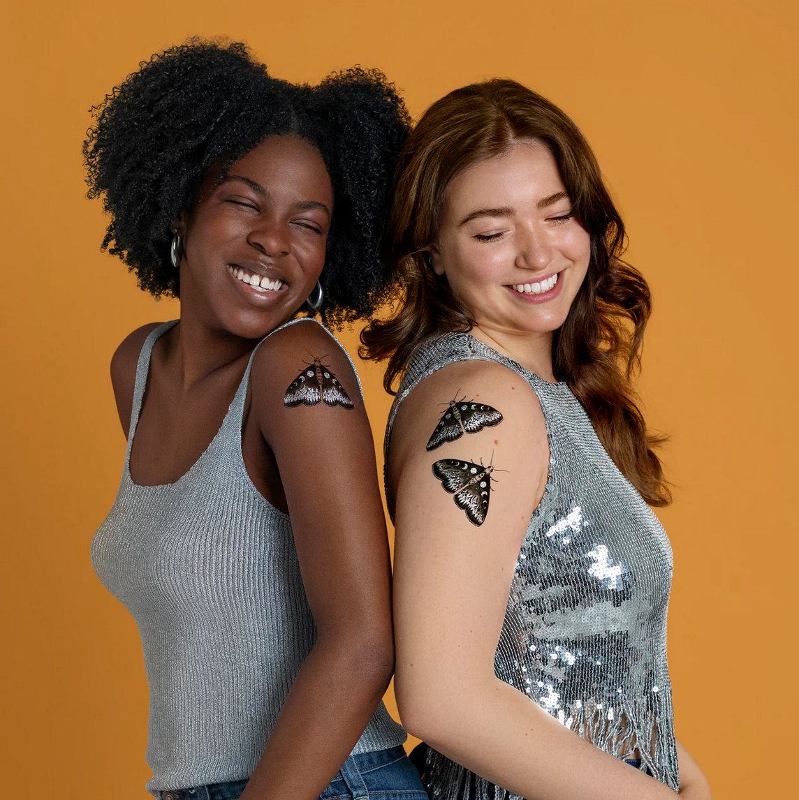Two women with moth tattoos on their arms against an orange background