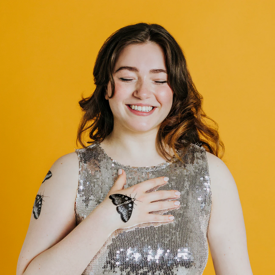 Woman wearing a sequin top with moth designs on a yellow background