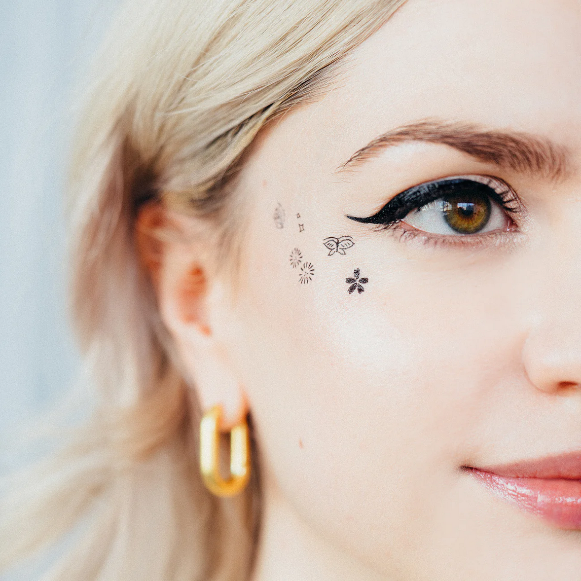Woman with temporary tattoos on her face, including butterflies and flowers.