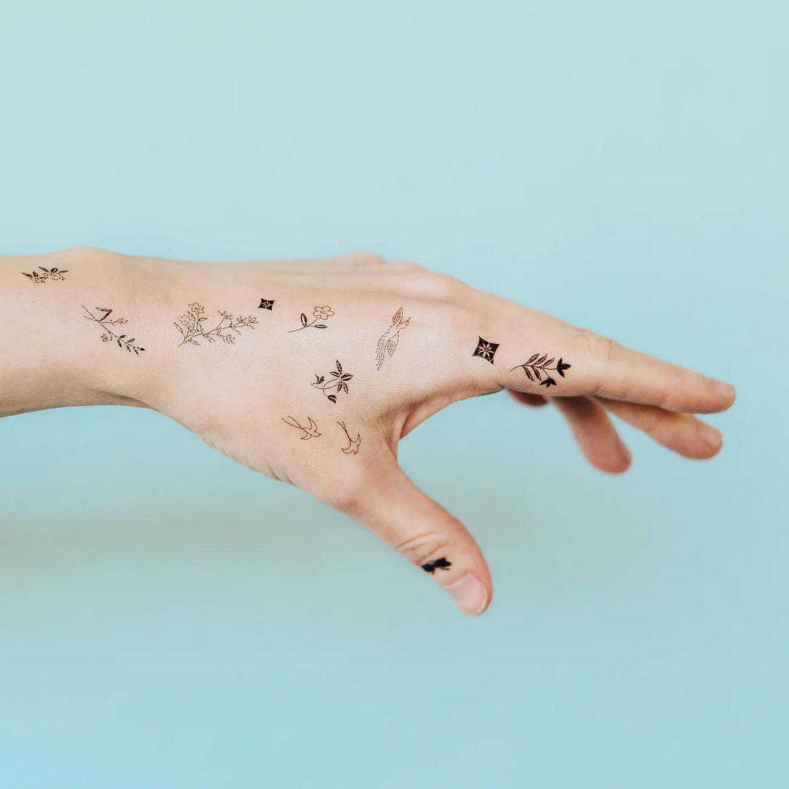 Hand with small temporary tattoos on a light blue background