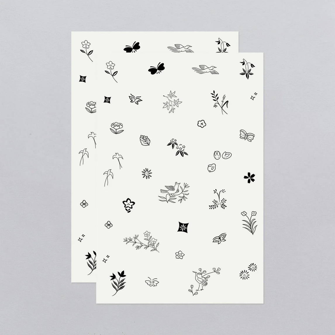 Two sheets of black floral and nature-themed temporary tattoos on a gray background