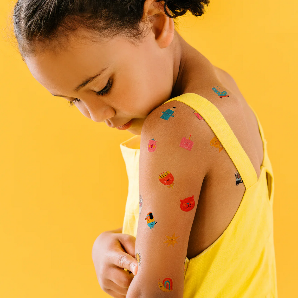 Child with colorful temporary tattoos on a yellow background