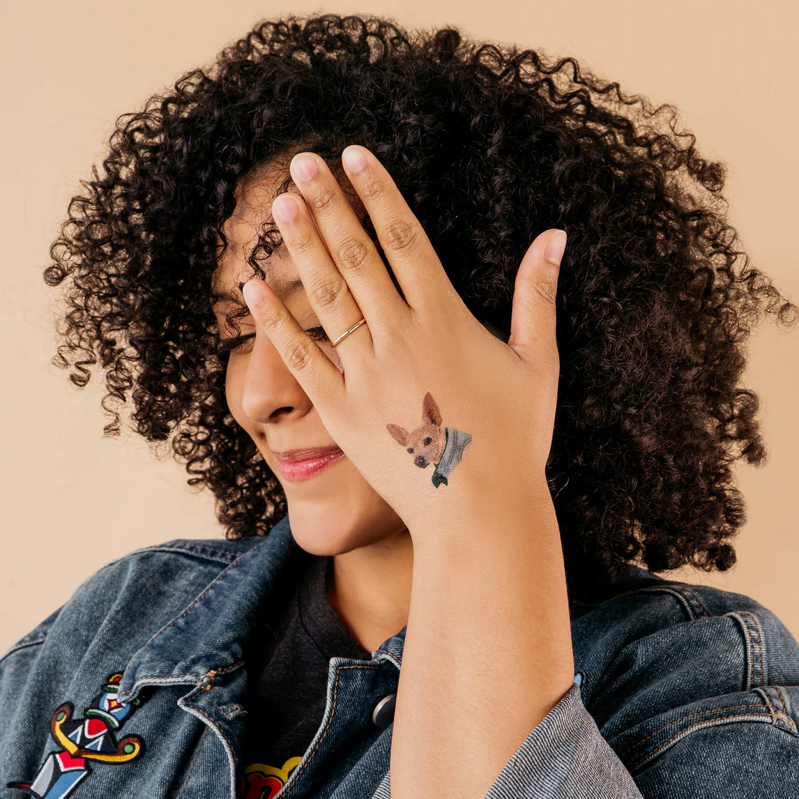 Woman with a tattoo of a dog on her wrist, wearing a denim jacket.